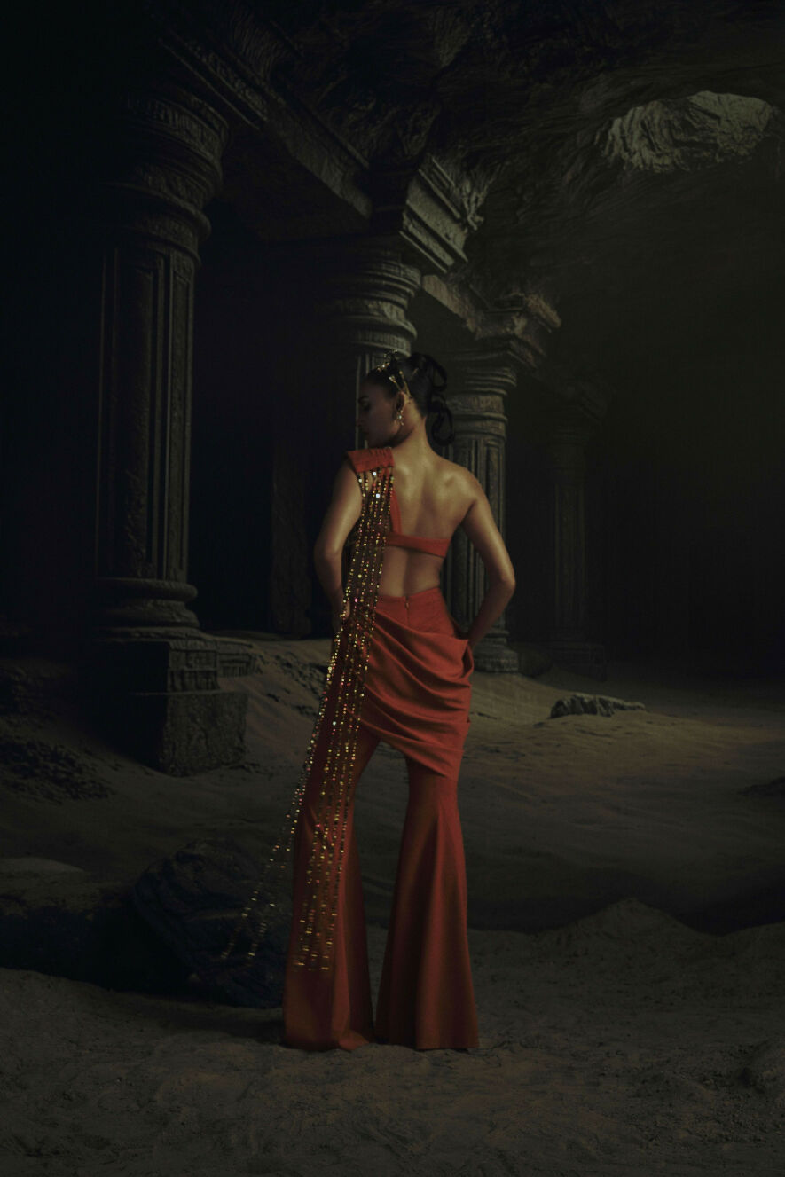 Woman in a red dress with gold accents standing in a dark, ancient ruin.