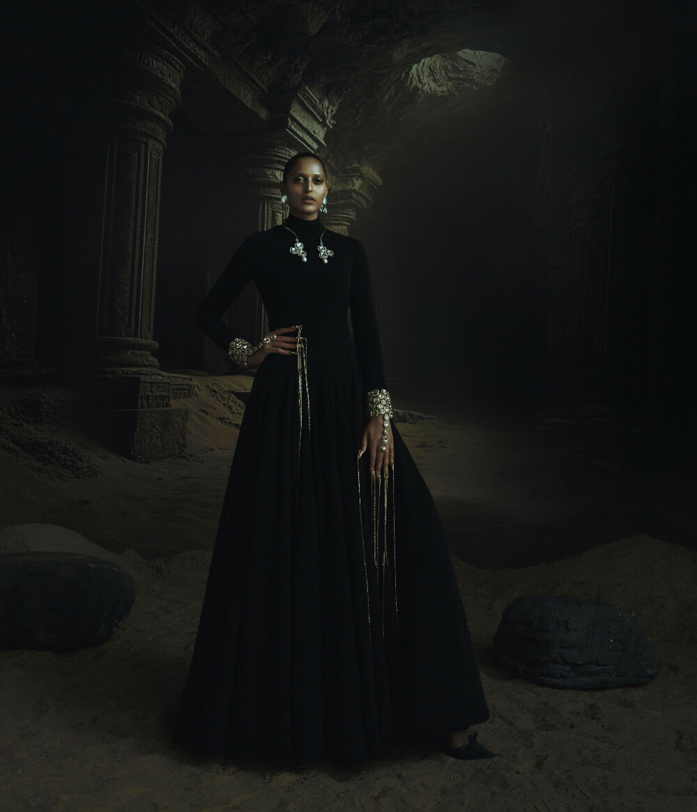 Woman in a long black dress standing in a dark, possibly ancient setting.