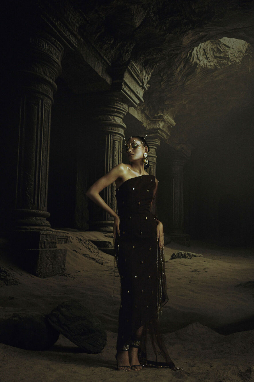 Woman in a dark dress standing in a dimly lit, ancient ruin.