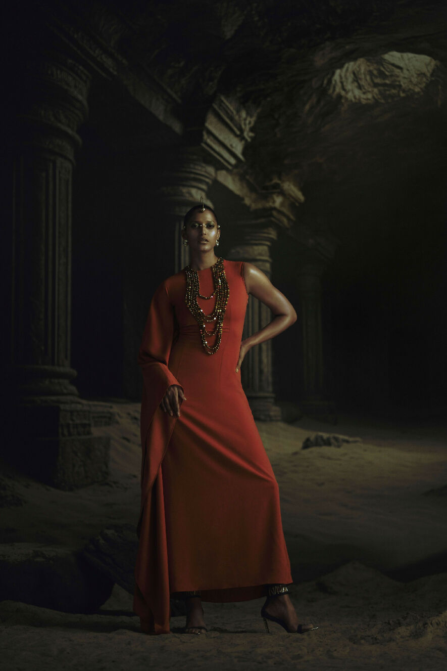 Woman in a red dress standing in a dark, ancient ruin.