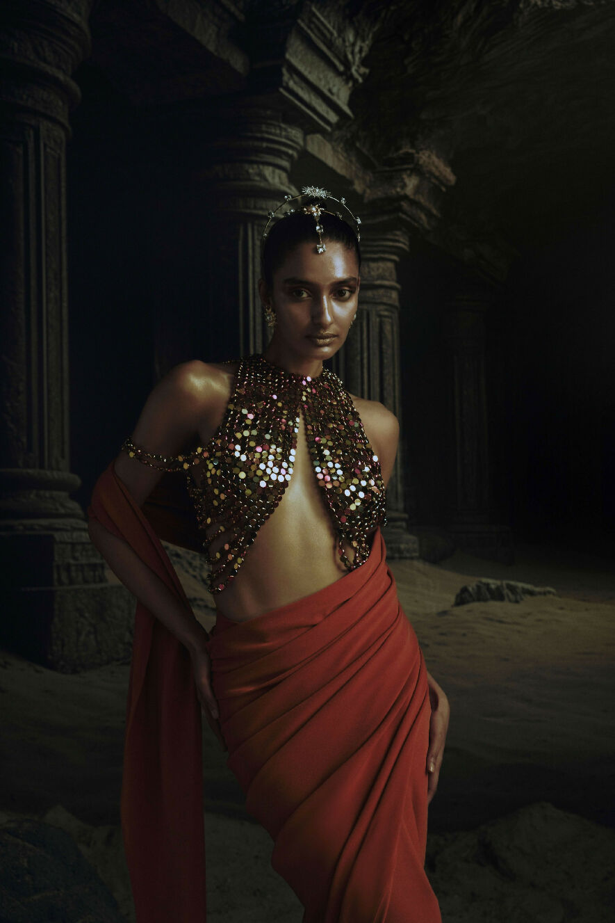 Woman in a red dress with a beaded top in a dark, possibly ancient setting.