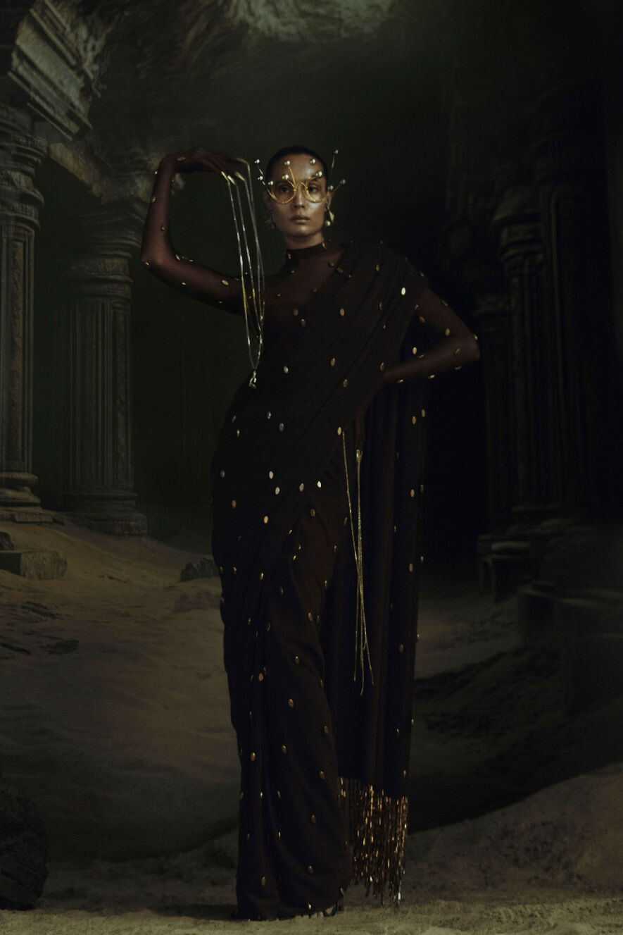 Woman in a black saree with gold details standing in a dark, ancient ruin.