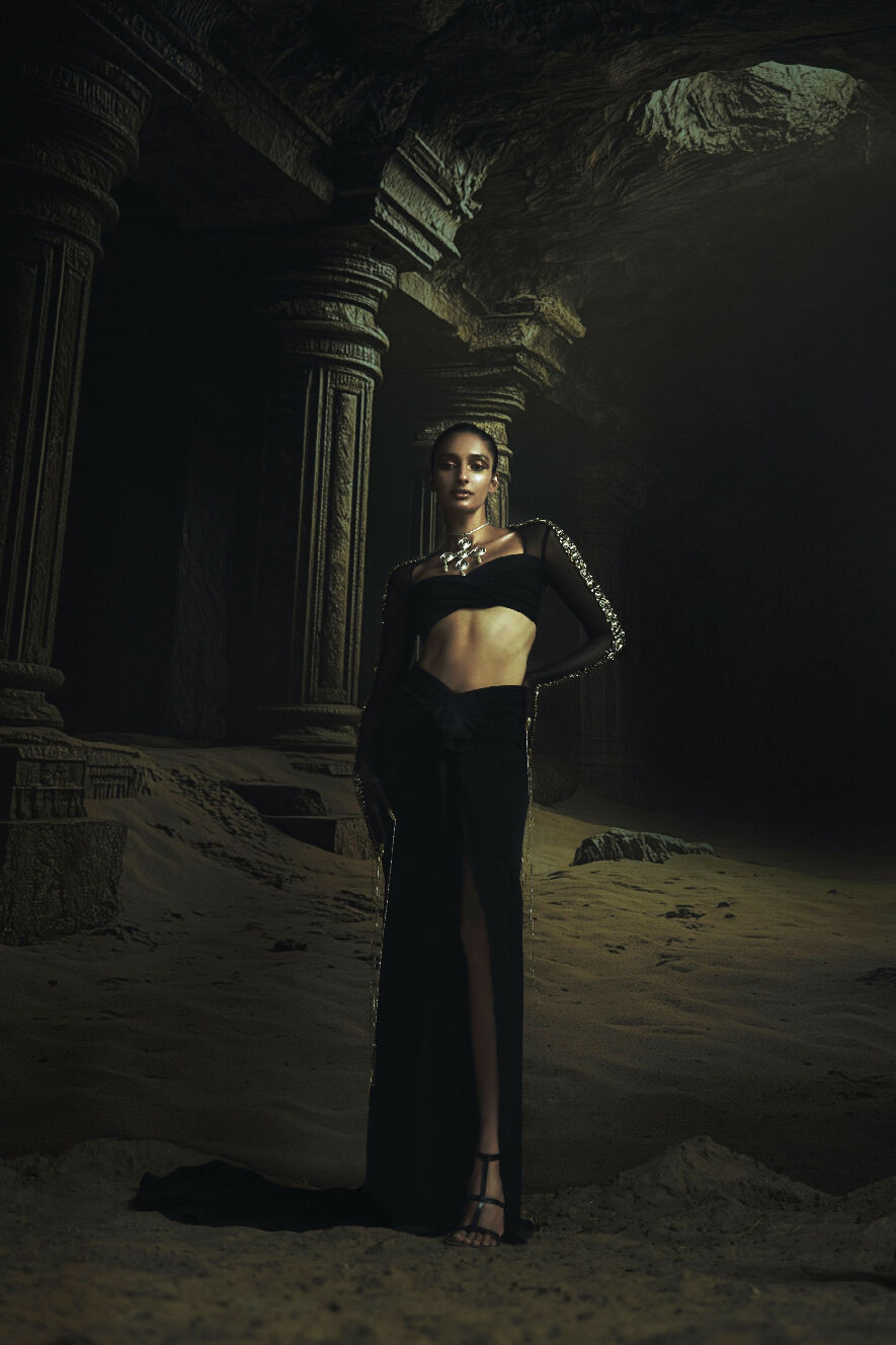 Woman in a black dress standing in a dark, ancient temple-like setting