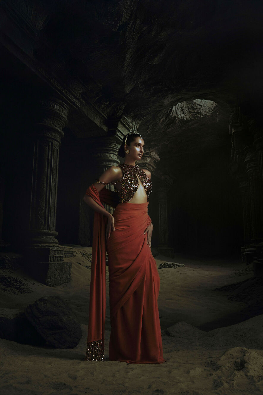 Woman in traditional attire standing in a dark, cave-like setting