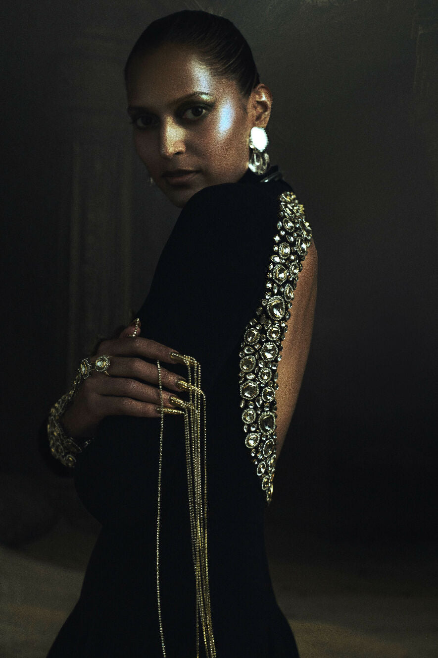 Woman wearing a black Kundan with intricate silver detailing and gold jewelry against a dark background