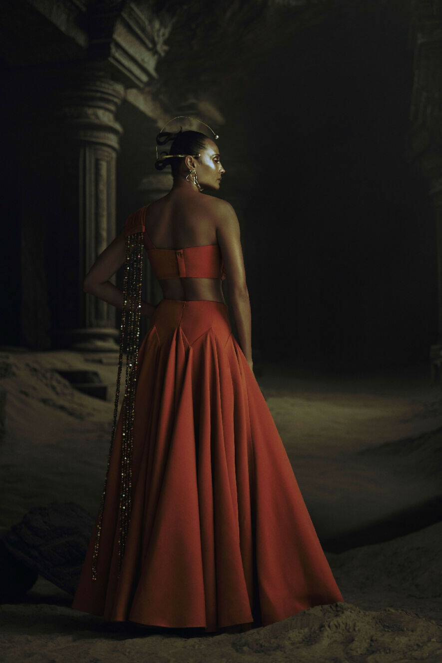 Woman in a red dress standing in a dark, sandy environment with columns.