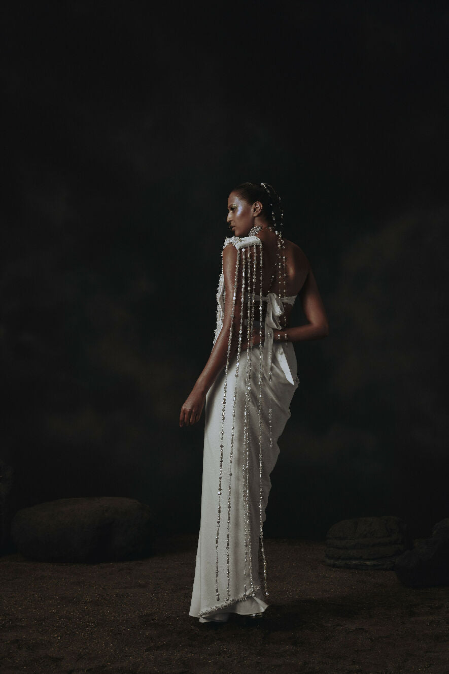 Woman in a white dress with beaded details standing against a dark background