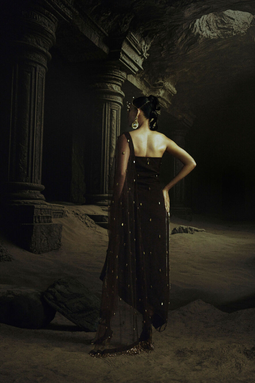 Woman in a dark dress standing in a dimly lit, ancient ruin-like setting.