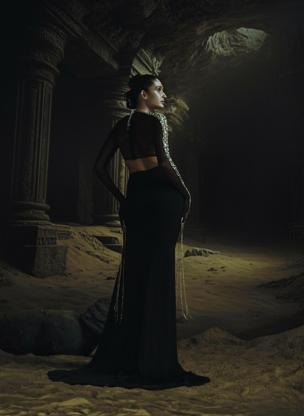 Woman in a black open back dress standing in a dark, ancient ruin.