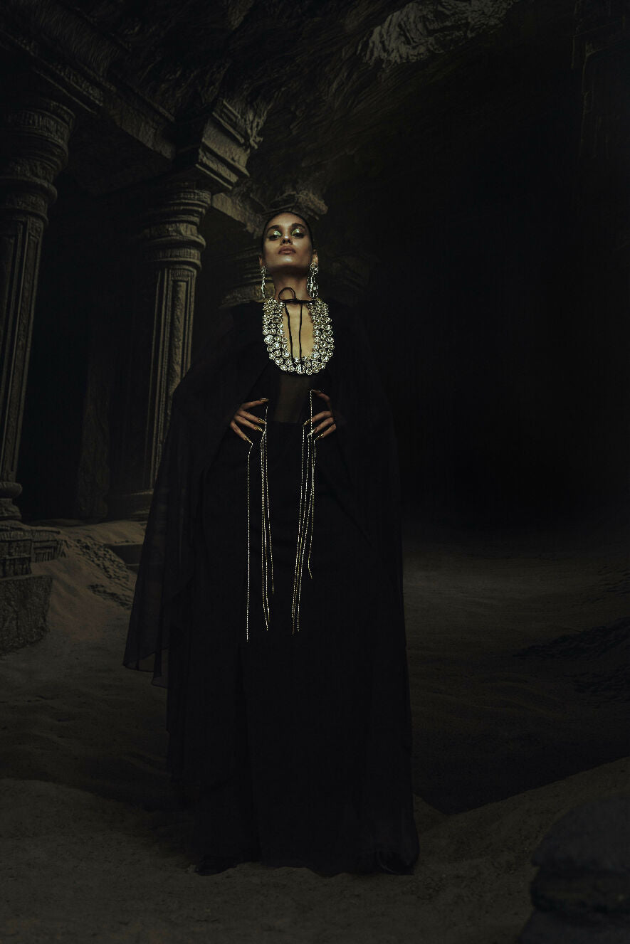 Person in a dark, ornate Kundan standing in a dimly lit, possibly ancient setting.