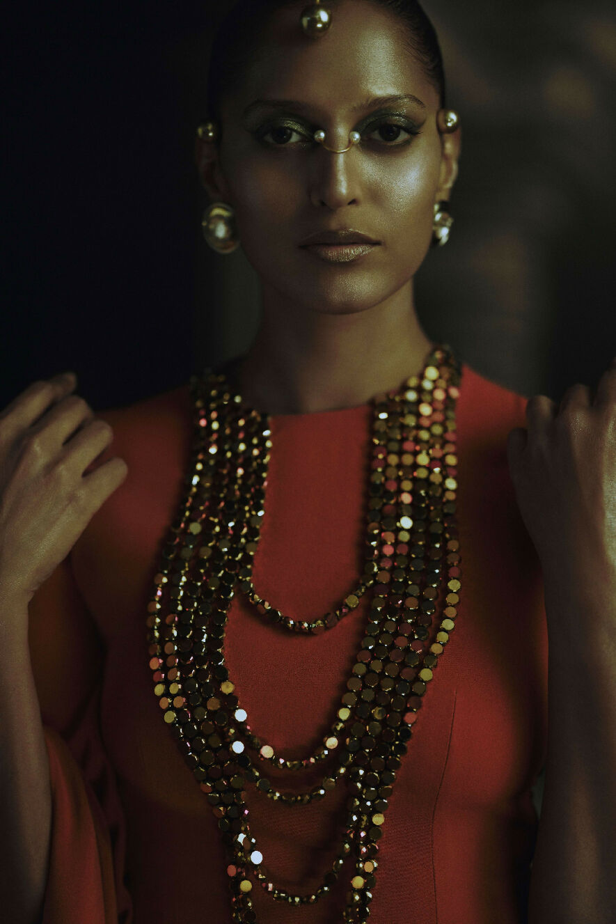 Woman wearing a red top and multiple beaded necklaces with a dark background