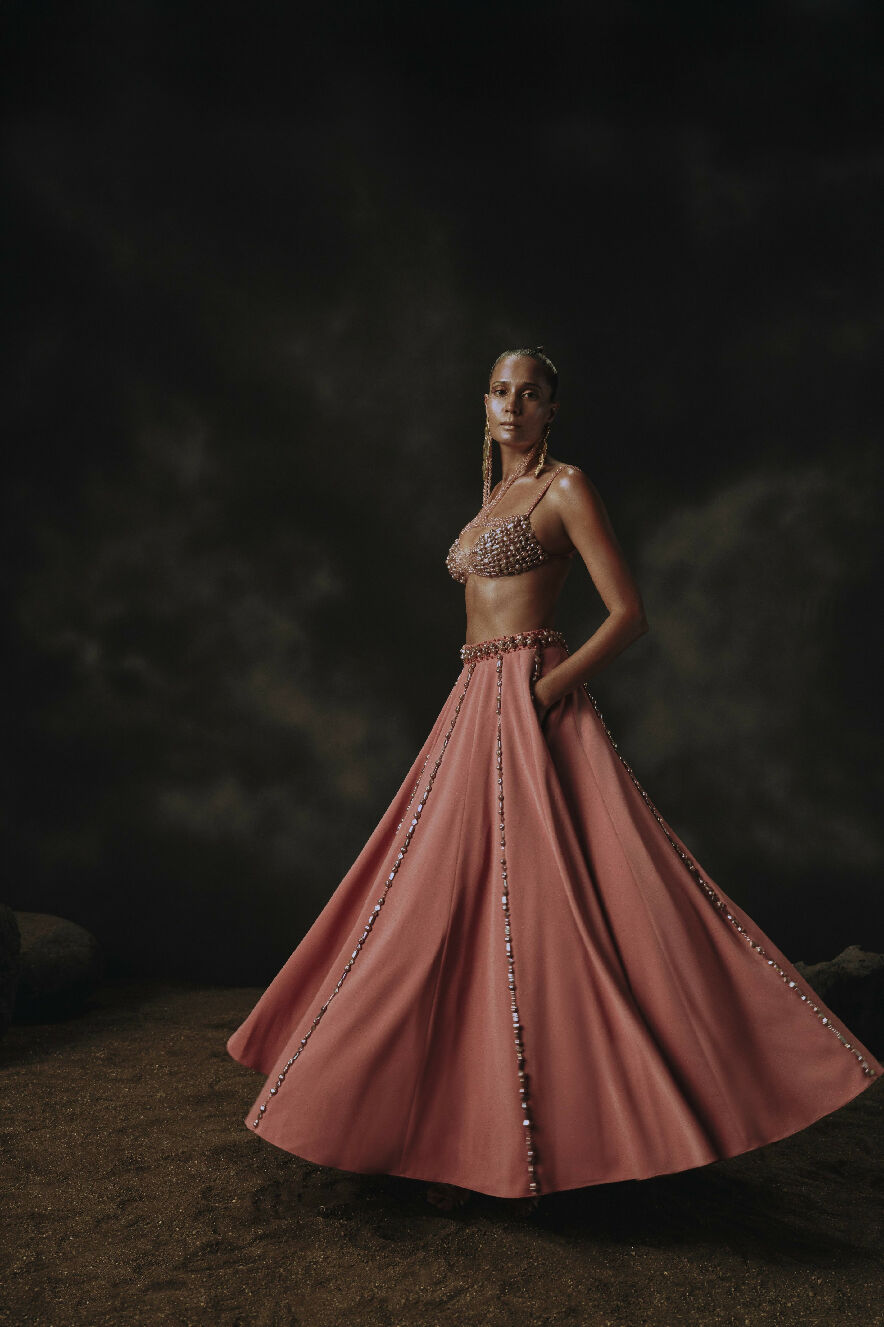Model wearing a pink evening gown with intricate detailing against a dark background