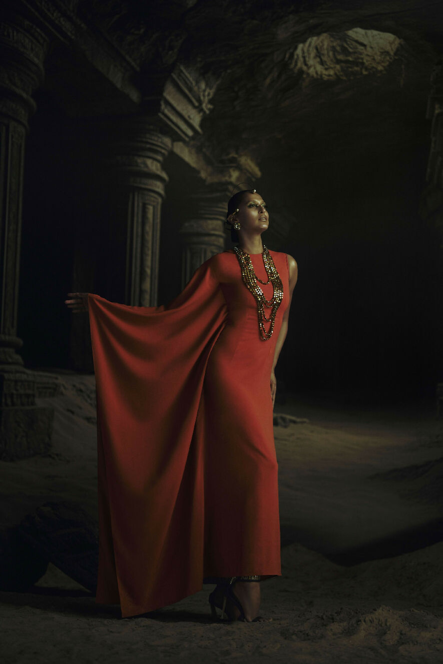 Woman in a red dress standing in a dark, ancient temple-like setting